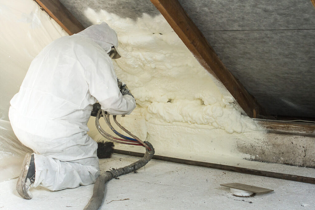 Man installing spray foam insulation in attic