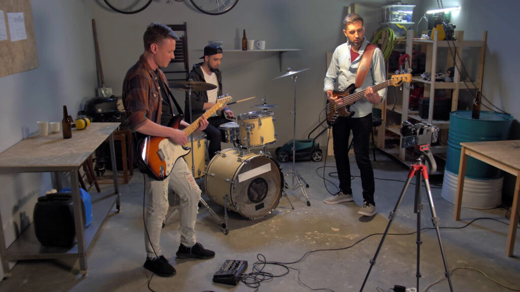 A band practices in a garage with a cement floor and gray walls