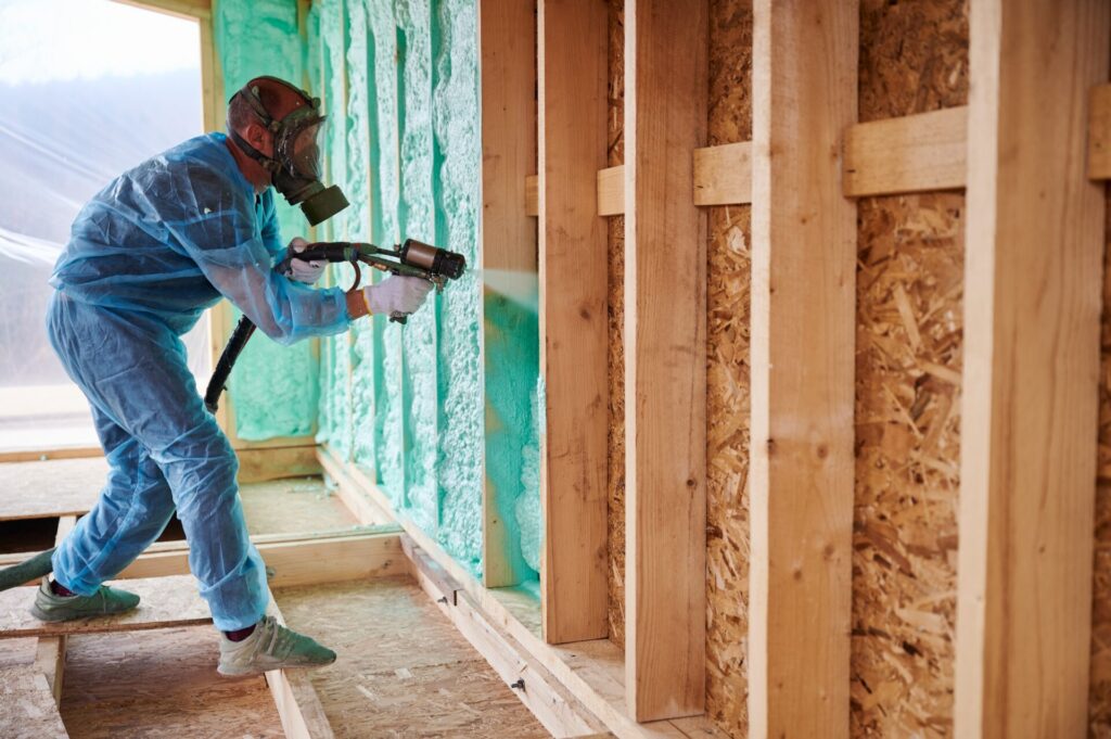 An installer in personal protective equipment installs spray foam insulation