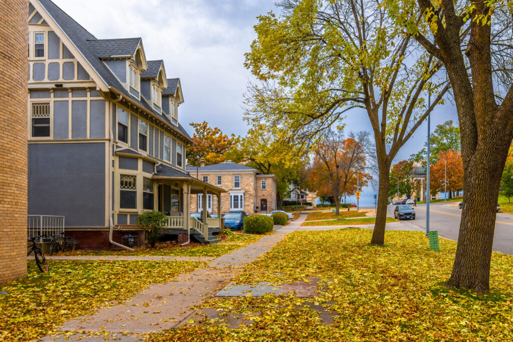 A Wisconsin street in the fall with yellow leaves covering the ground in front of a blue house