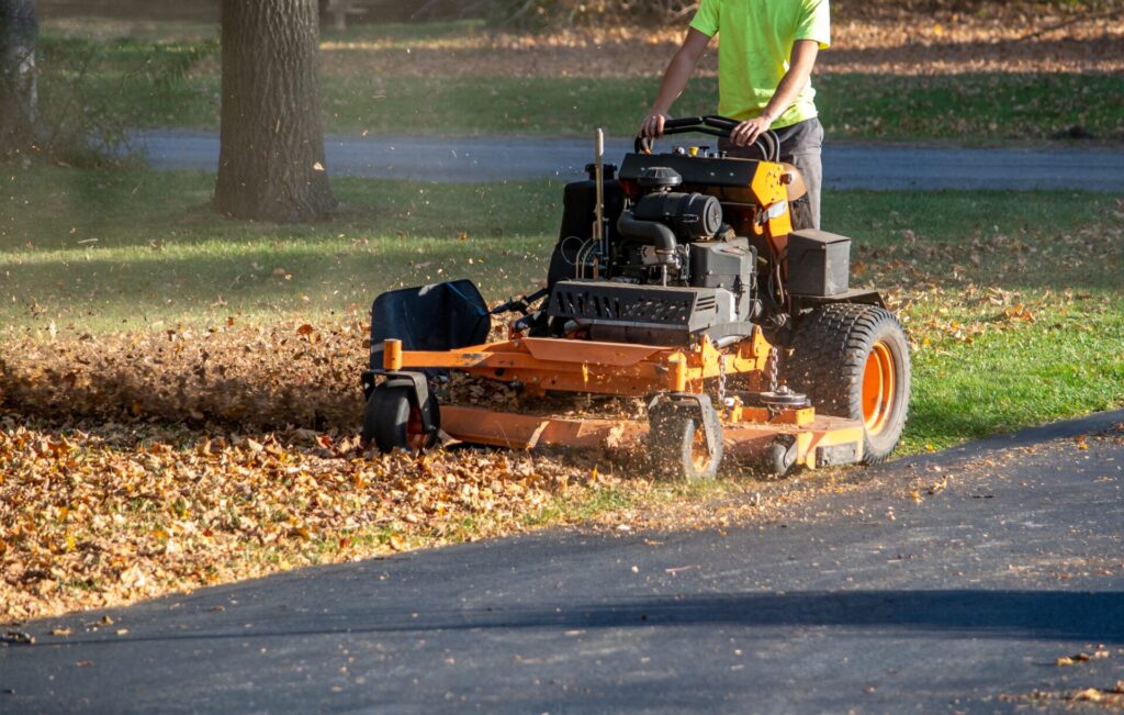 A worker stands on a riding mower that helps to tear up leaves for a lawn clean up
