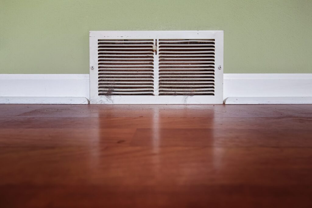 A dust air register wall vent on a green and white wall