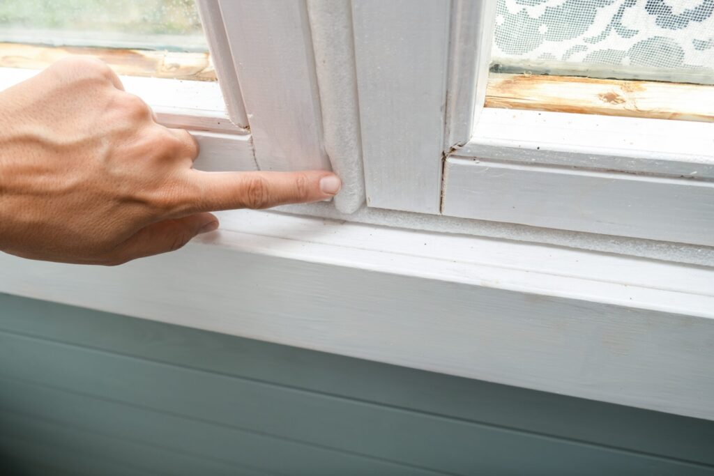 A hand inspects the space around a white window frame