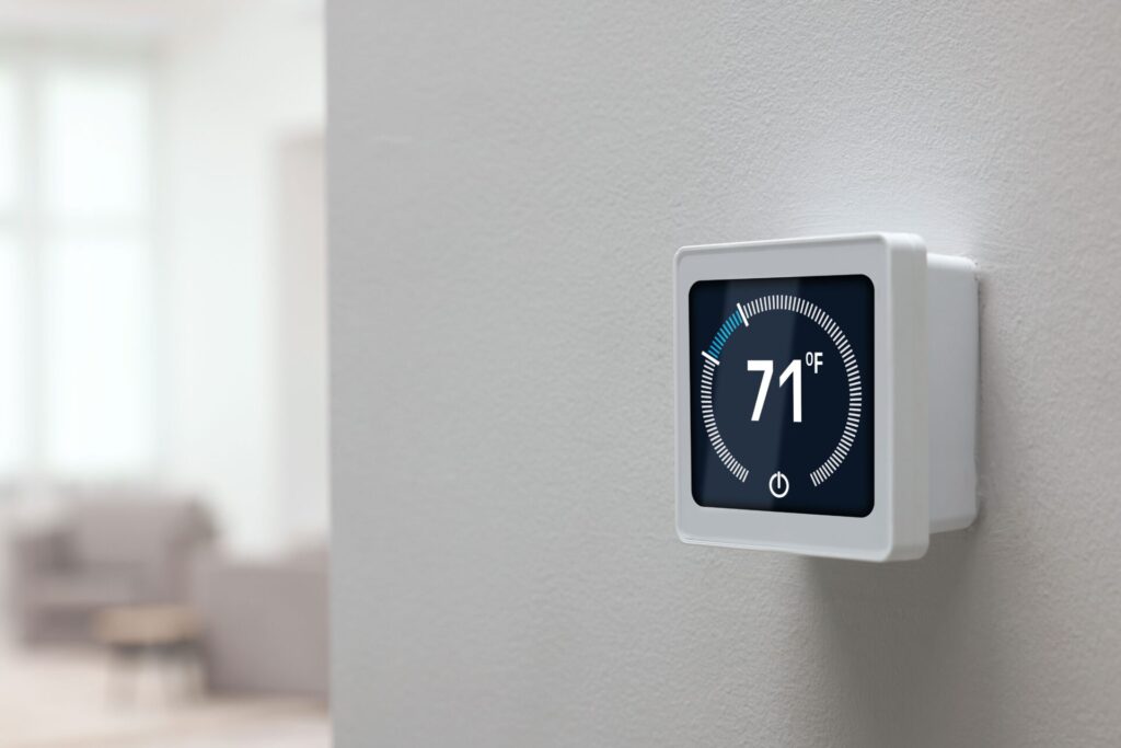 A smart thermostat displaying a temperature of 71 degrees mounted on a white wall