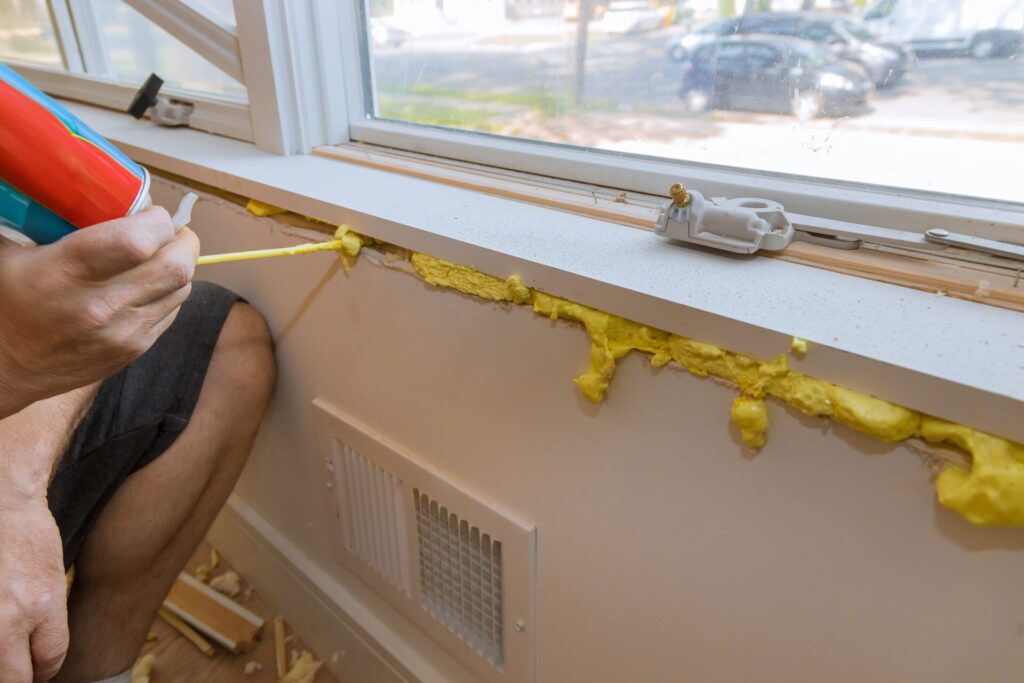 Yellow spray foam insulation being installed from a handheld canister around a window frame